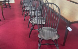A set of 8 handcrafted American Windsor side chairs featuring a historical bow back design. The chairs are finished in an antique black over red crackle paint, showcasing beautifully shaped seats and elegant turnings.