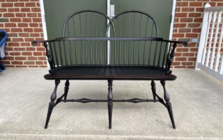 American Made Historical Double Sack Back Windsor Settee with turned legs, carved knuckles, and an antique black over red crackle finish.